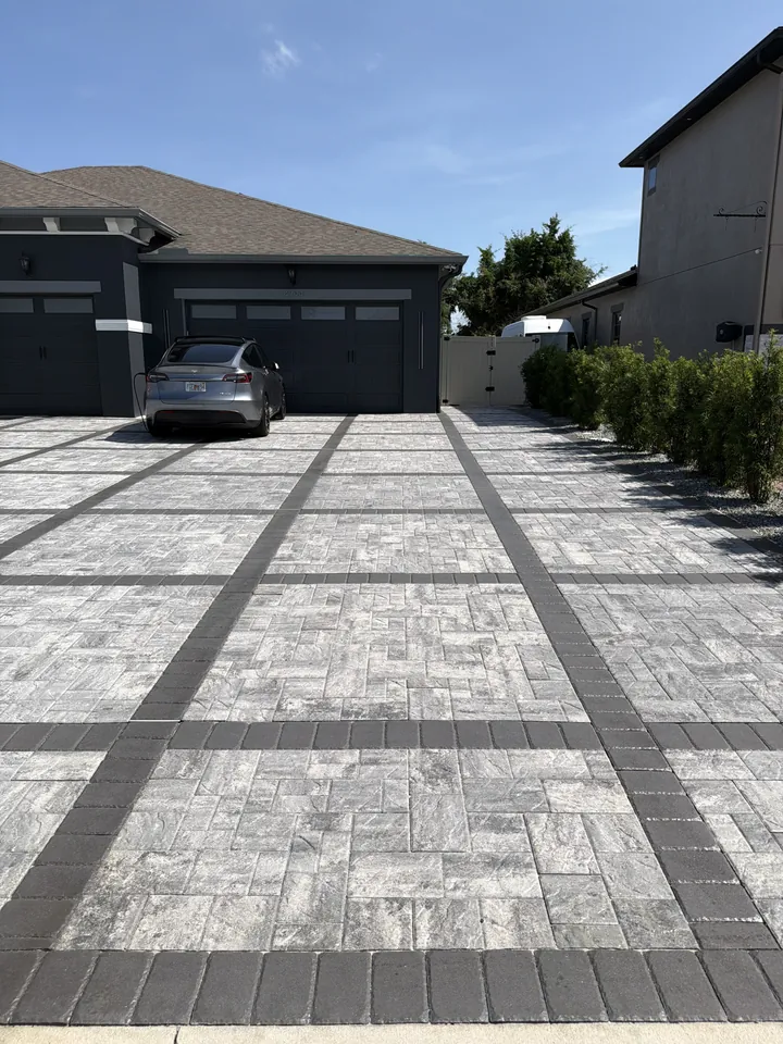 Approach to a dark garage door over gray pavers with charcoal bands and a paver walk splitting off to the side