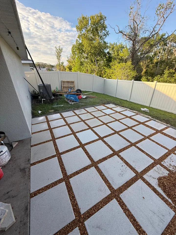 Patio of oversized square concrete pavers with pea-gravel joints on a compacted base behind a house