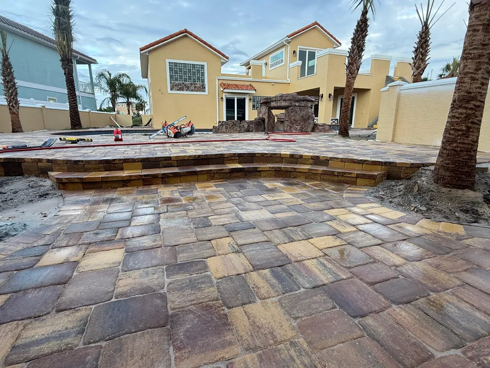 Two-level paver patio mid-build: raised pool terrace, paver-faced risers, wet saw on the lower level