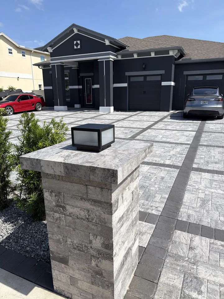 Entry pillar faced in the same gray and charcoal pavers as the driveway, with a lantern mounted on its face