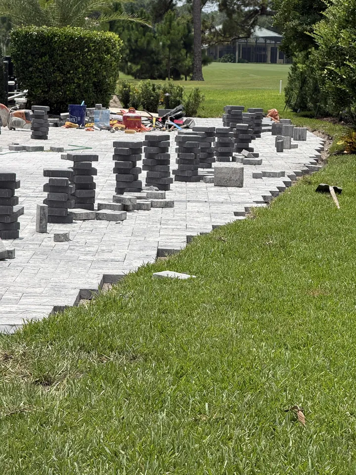 Cubes of pavers staged beside a driveway under construction, the sand bed screeded level to the lawn edge