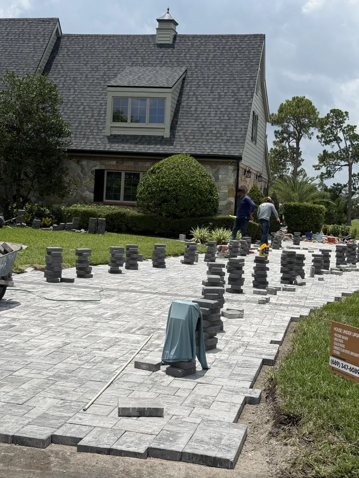 Crew laying a paver driveway field from stacked cubes staged on the screeded sand bed