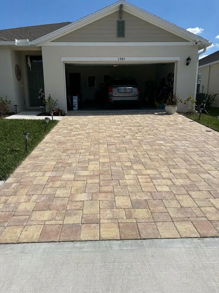 Tan-blend paver driveway ending at a poured concrete apron where it meets the street